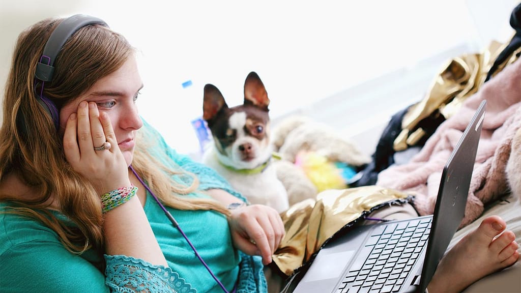 Young woman using a laptop, sitting with a small dog